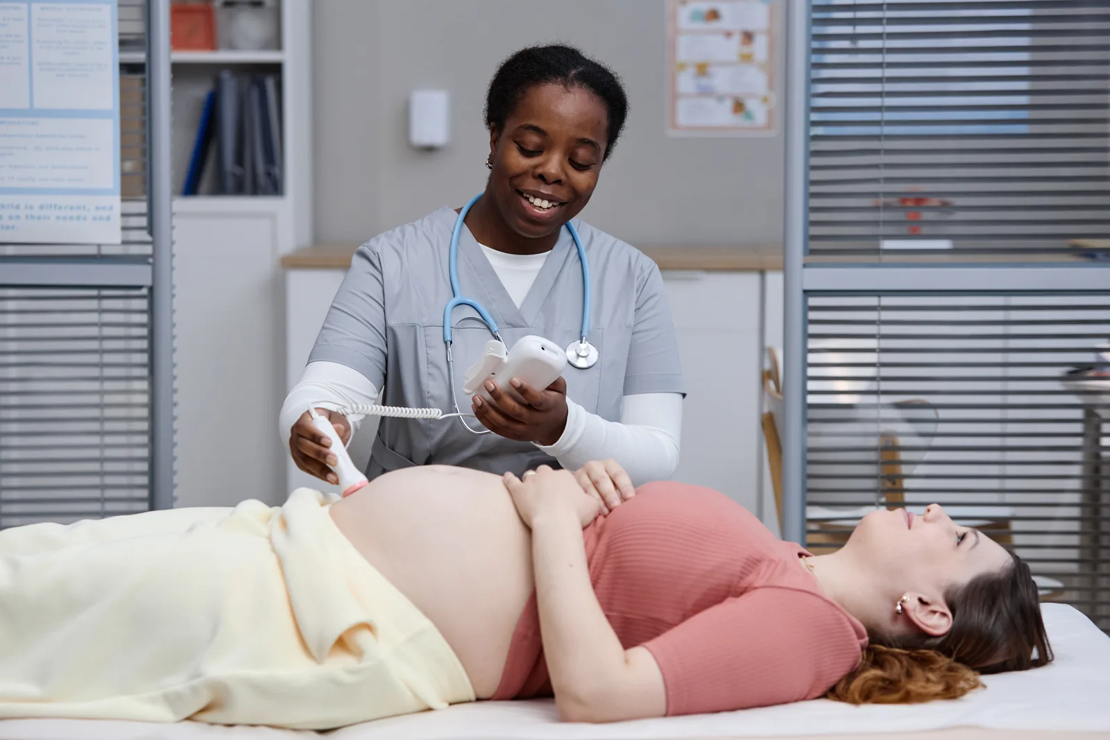 A midwife checks a pregnant client's belly with a fetal doppler during a prenatal visit