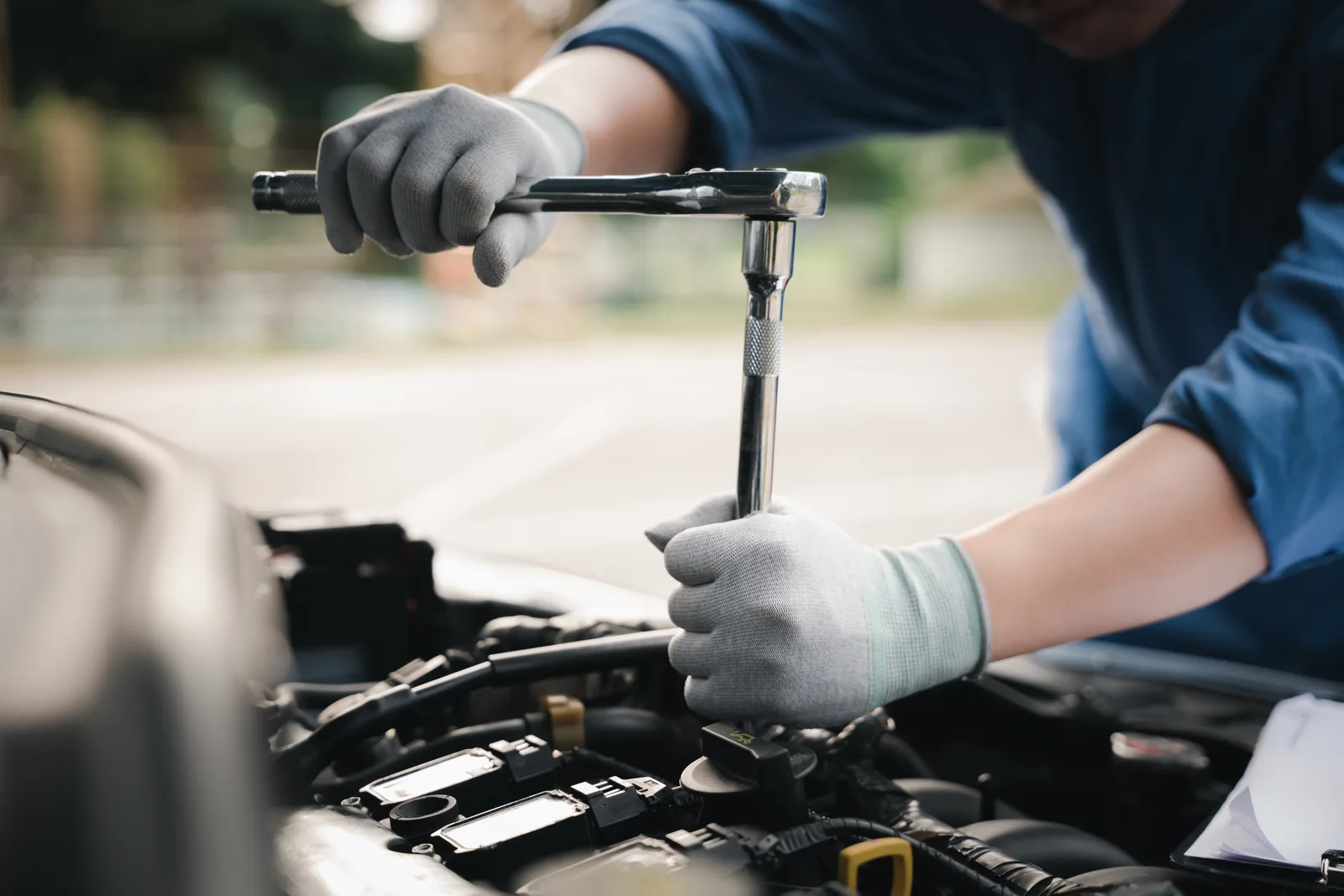 Mobile mechanic working under the open hood of a car in a customer's driveway beside his service van
