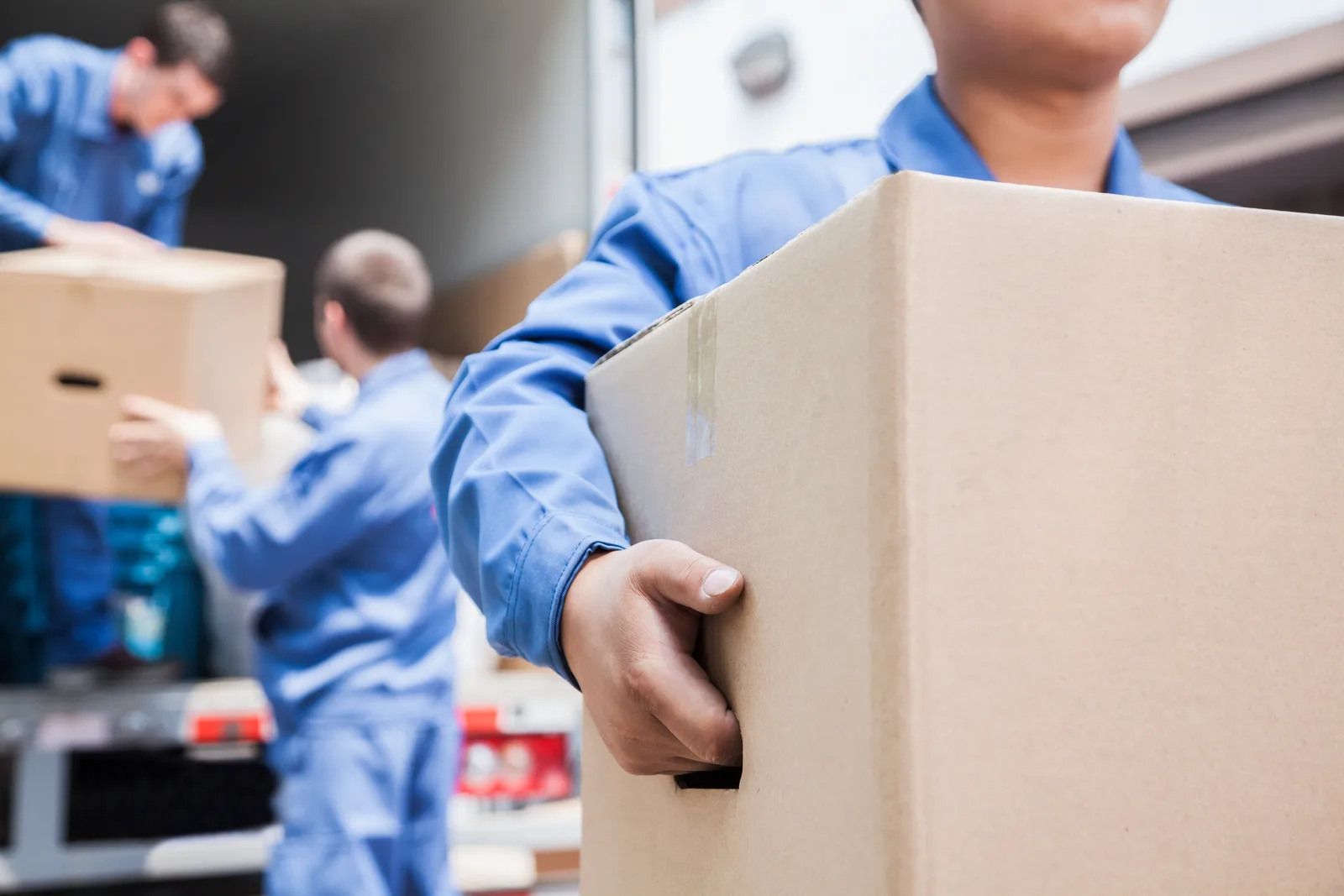 Two movers carrying labeled boxes down the ramp of a moving truck outside a customer's home