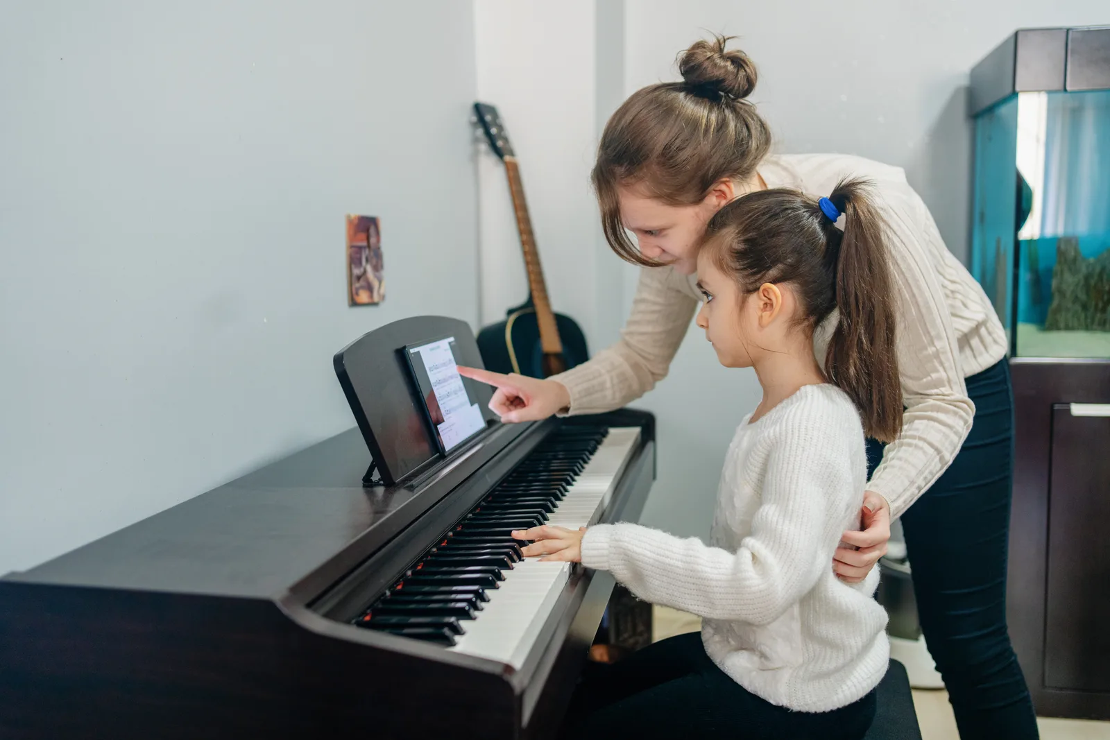 Piano teacher sitting beside a young student during a lesson at the keyboard