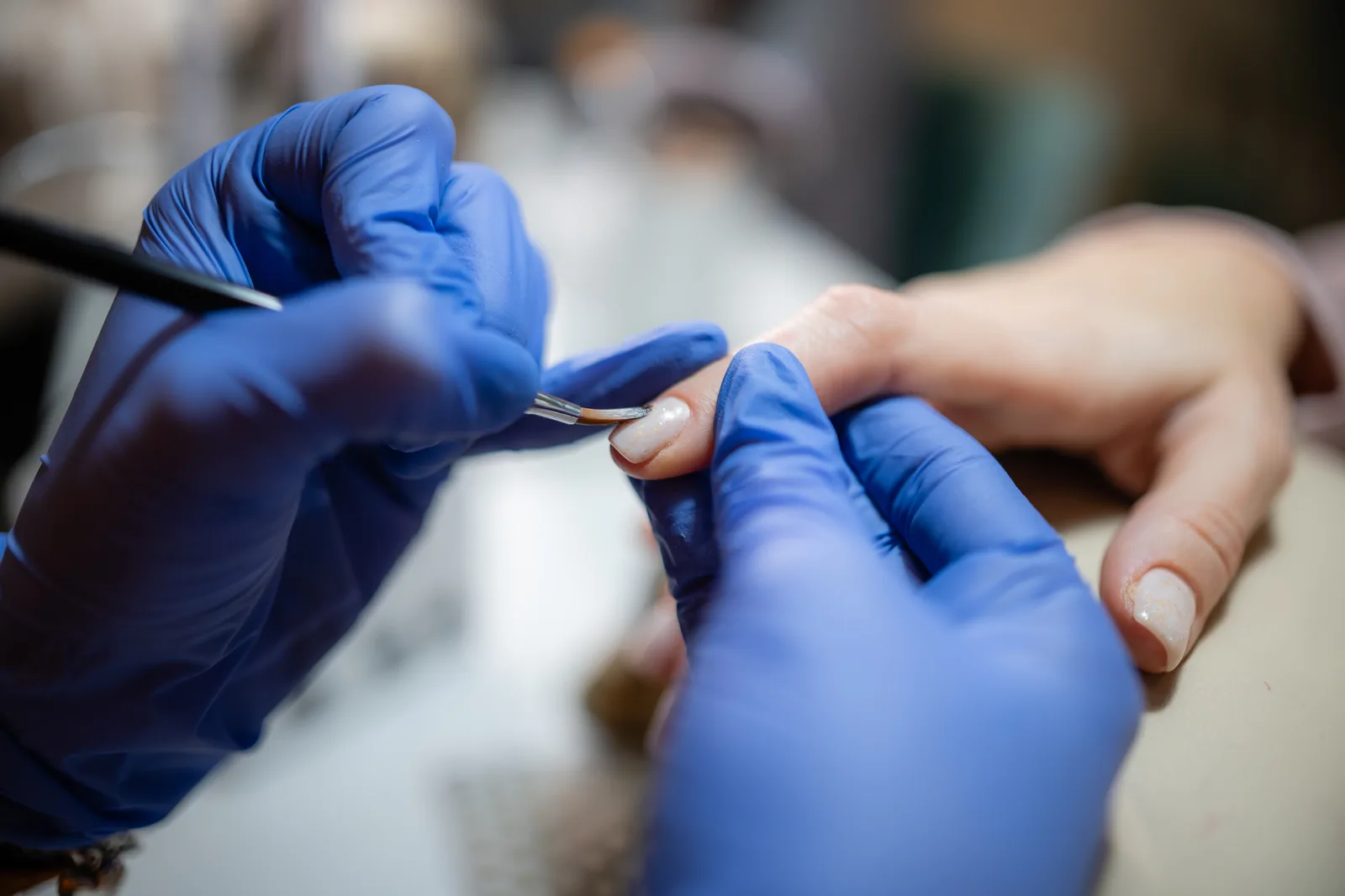 Nail technician painting a seated client's nails at a salon manicure table