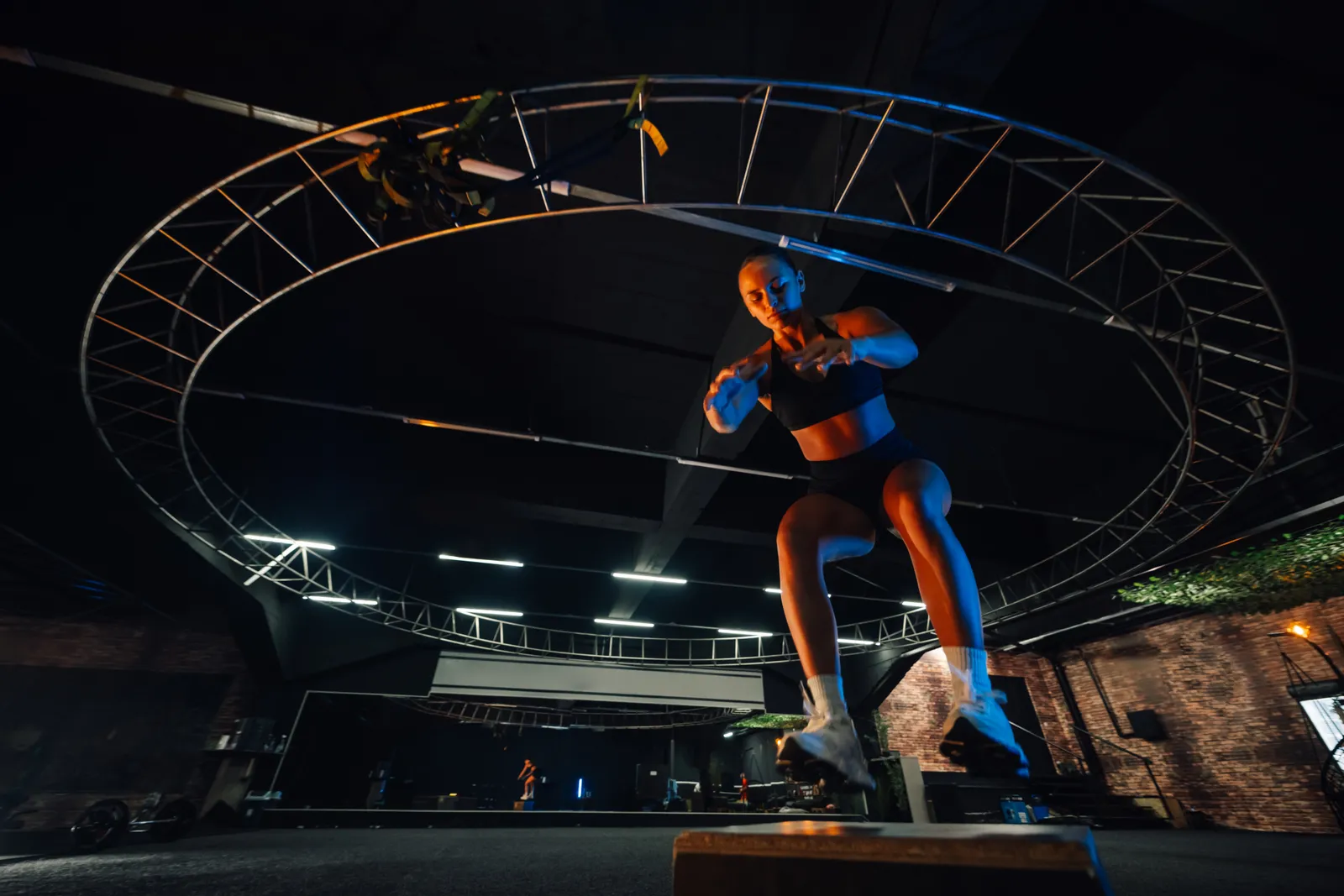 Ninja warrior gym athlete sprinting up a curved warped wall toward the top bar, with padded mats below in an indoor obstacle course gym