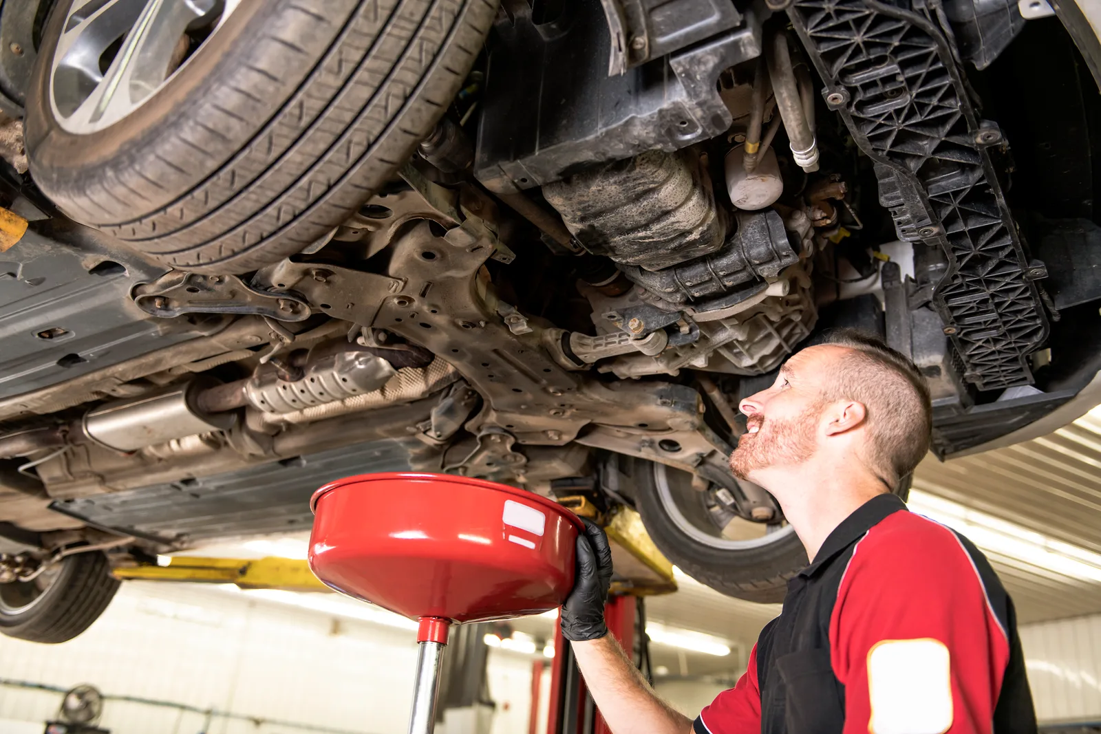 Technician draining engine oil from a car on a lift in a quick lube service lane