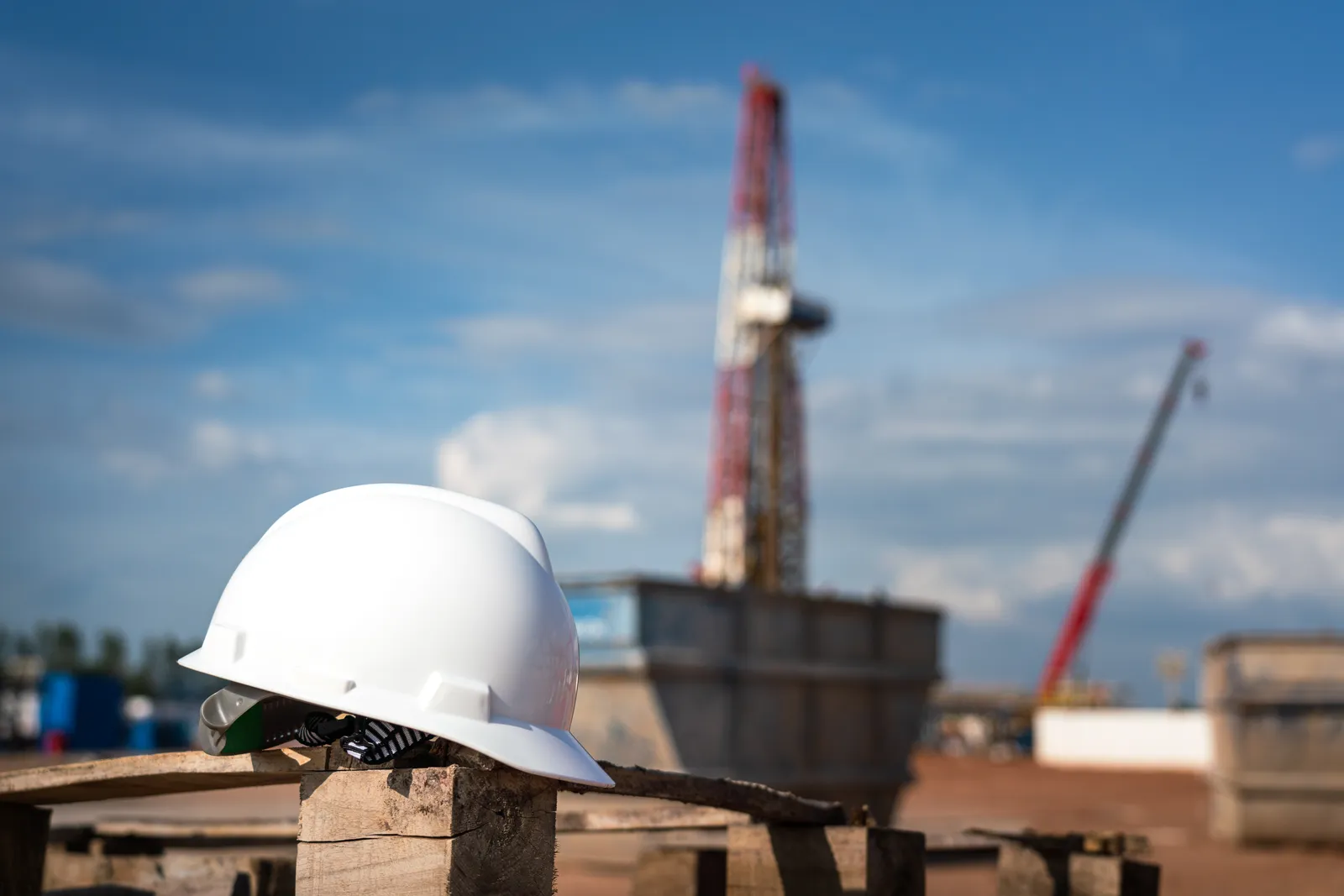 Hard hat resting at an oilfield with a drilling rig in the background