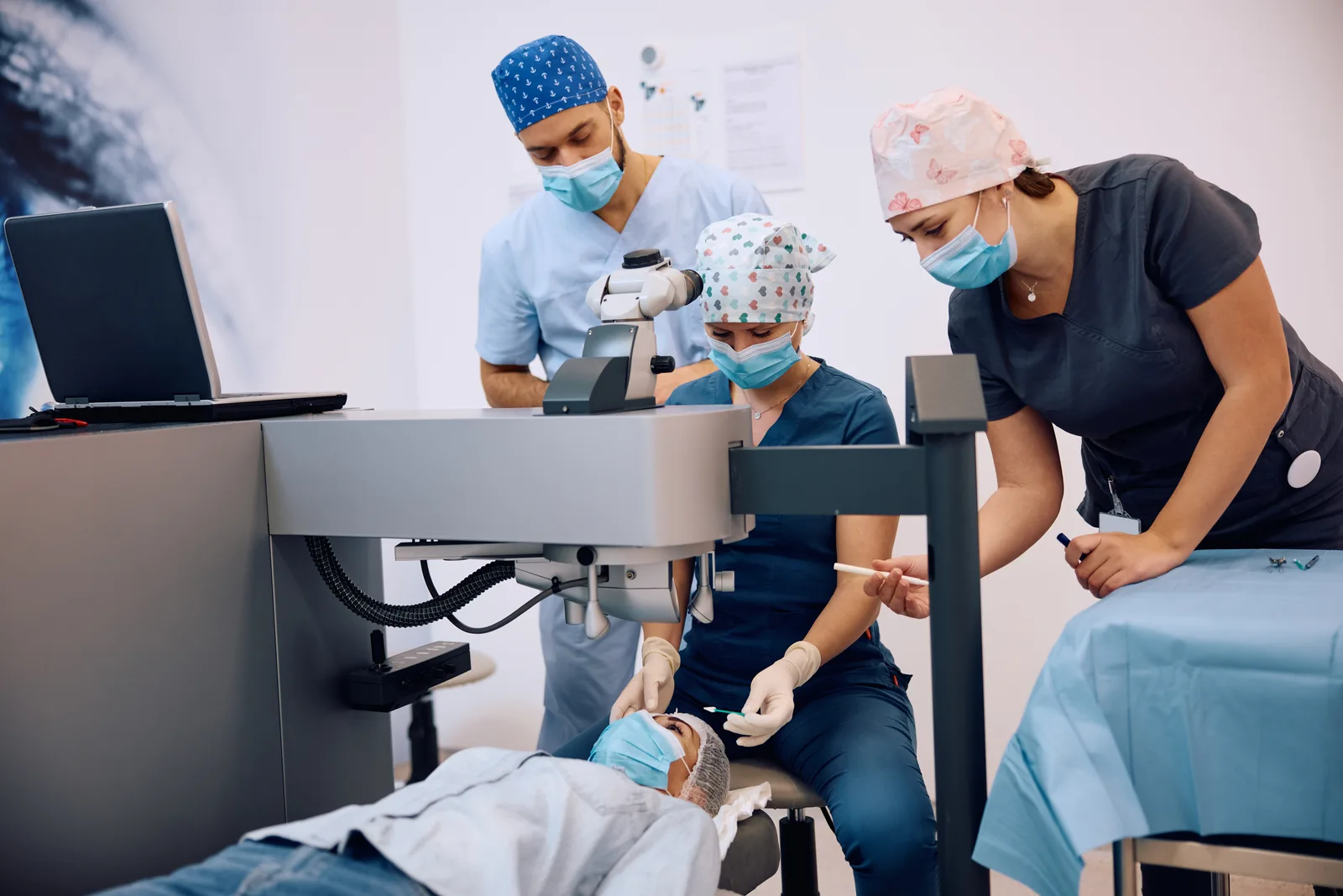 Eye surgeon in surgical attire performing laser eye surgery at an operating microscope