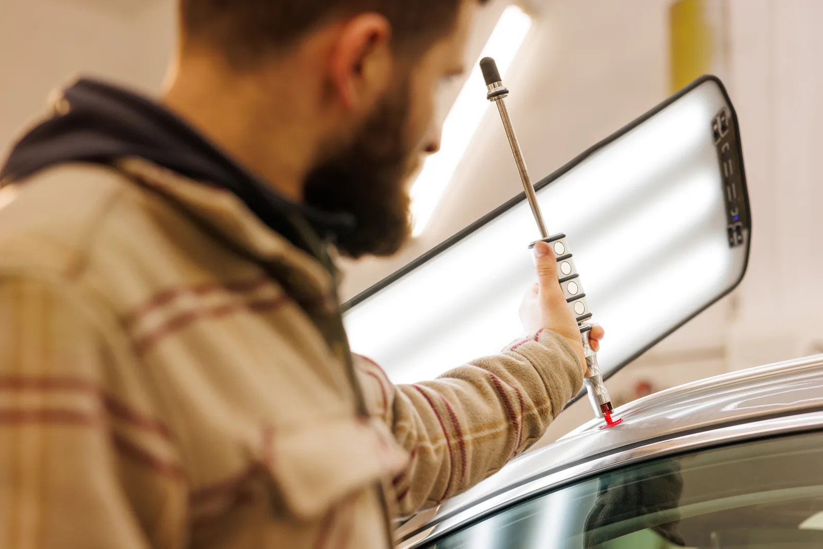 Paintless dent repair technician using a metal dent rod to gently push a hail dent out from behind a car door panel, leaving the factory paint untouched