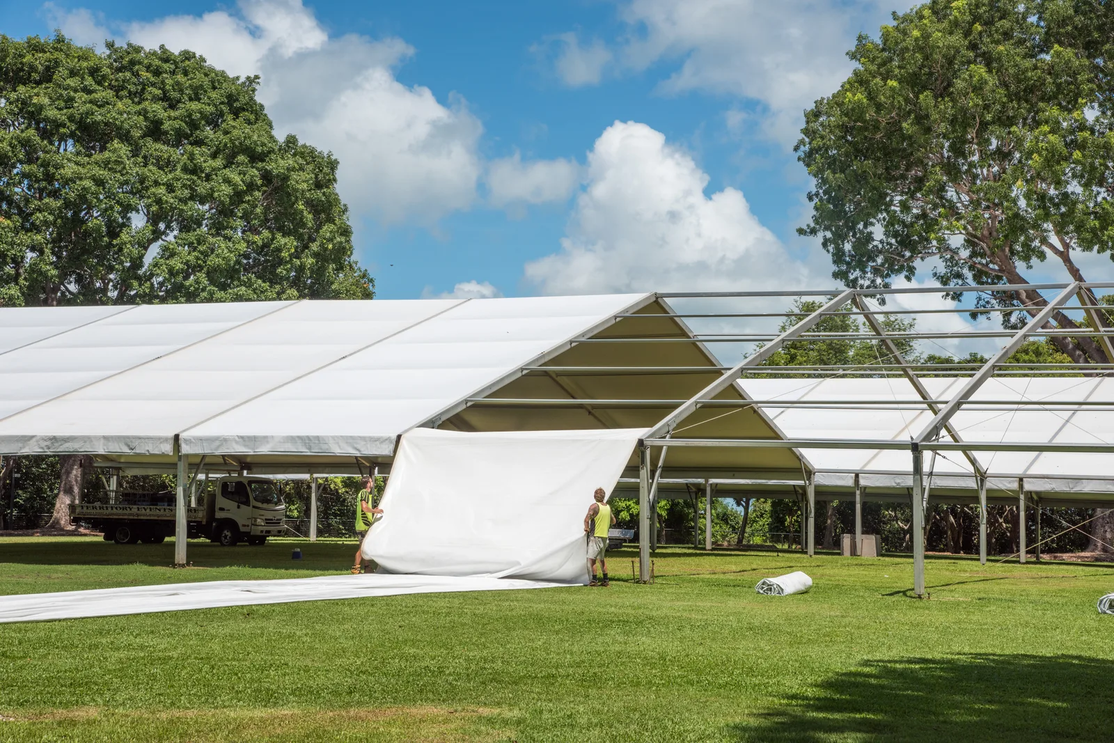 Party rental crew setting up a white event tent with tables and folding chairs on a lawn