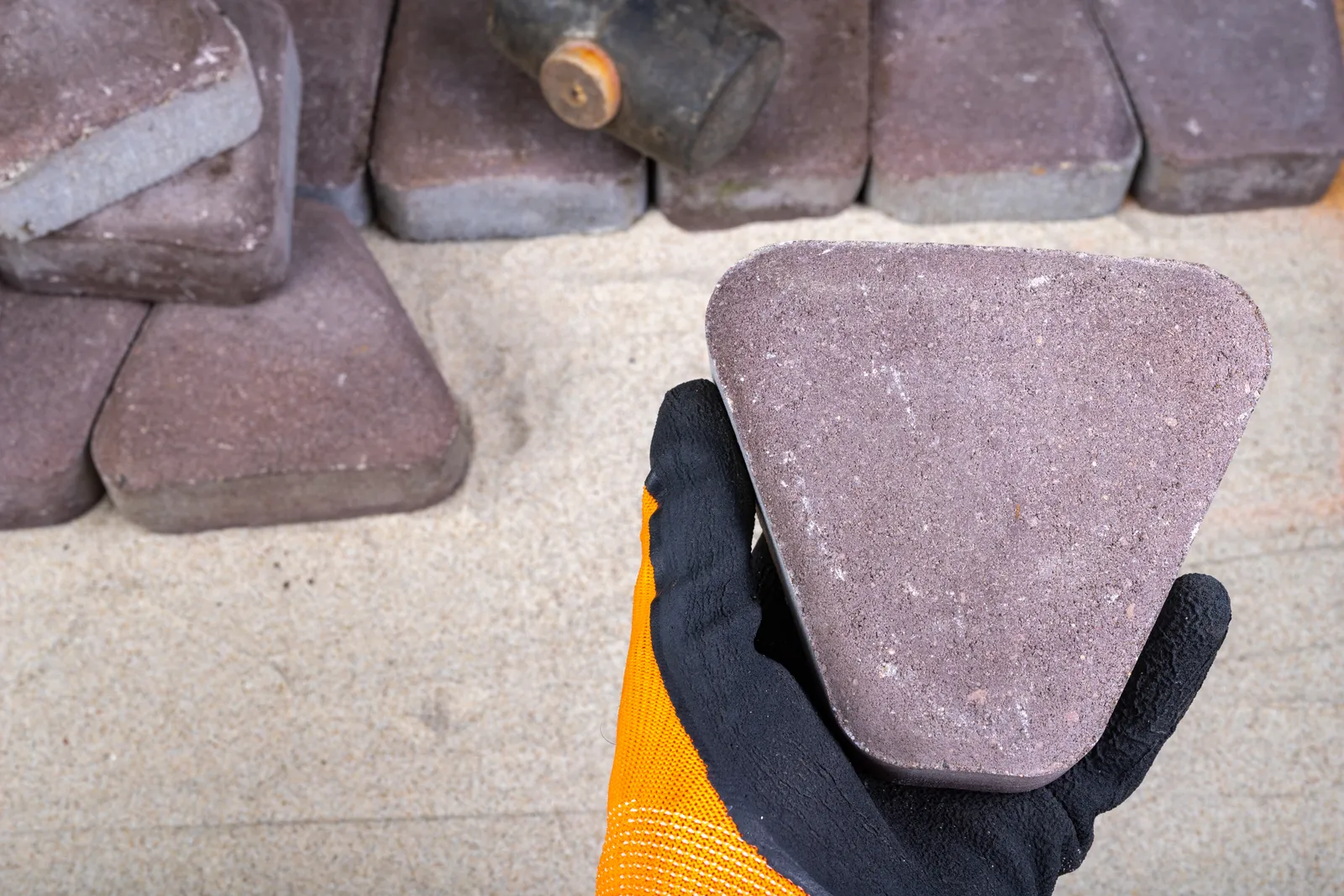 Hardscape installer setting interlocking pavers into a compacted sand base for a new backyard patio