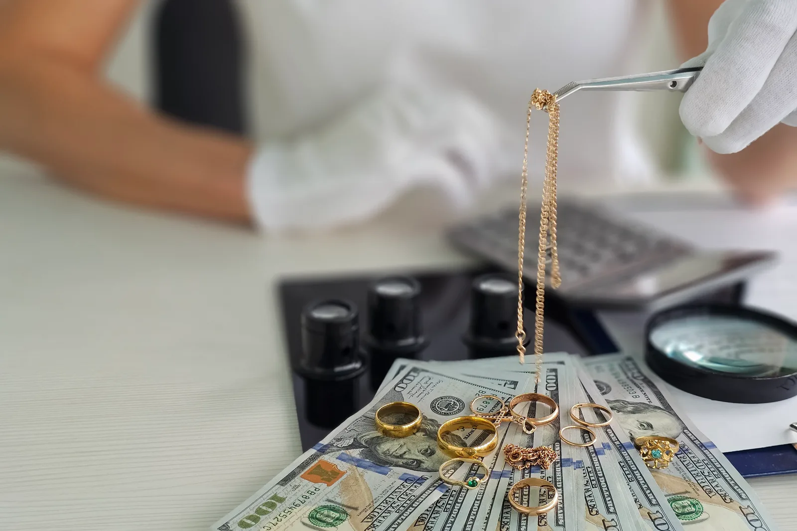 Pawnbroker examining a gold necklace with a loupe at the counter while a customer waits