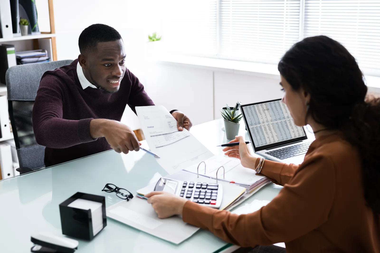 Payroll specialist reviewing a small business owner's pay run and tax filings together at her office desk