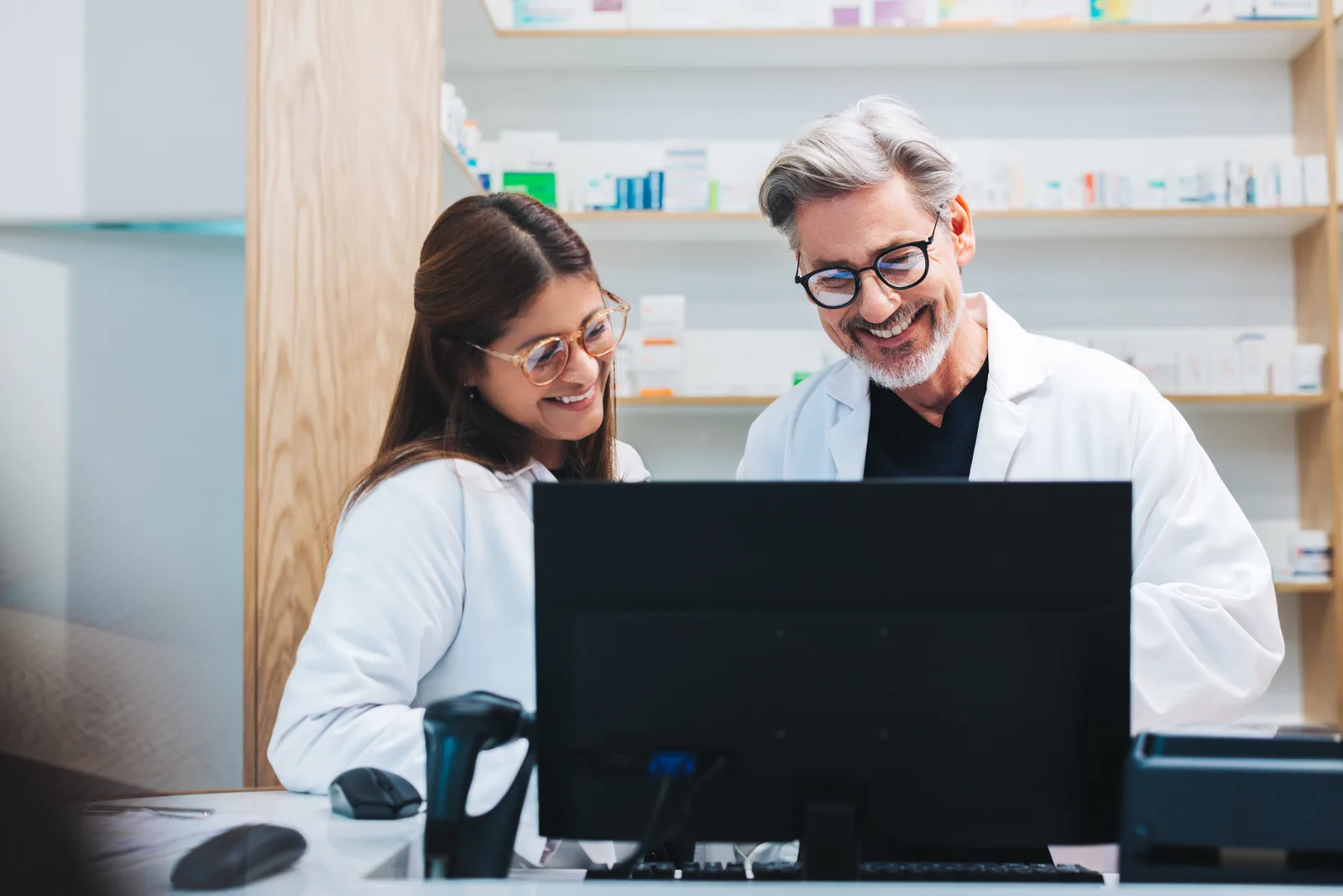 Pharmacist and pharmacy technician reviewing a prescription dispensing dashboard together at the pharmacy counter