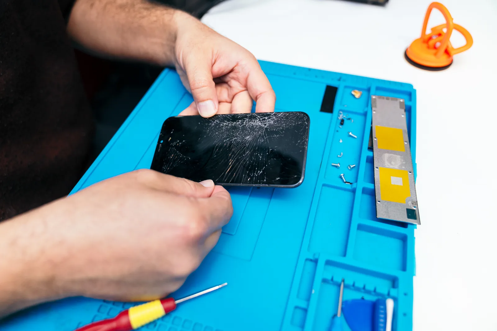 Phone repair technician replacing a cracked iPhone screen at a workbench with precision tools