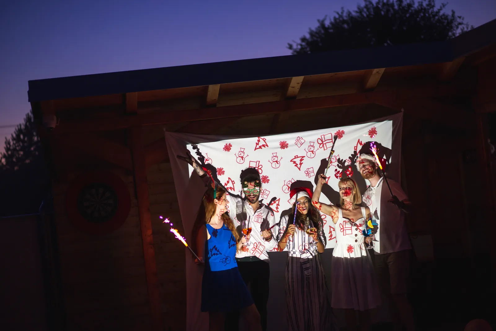 Guests laughing together inside an open-air photo booth surrounded by string lights and props at a wedding reception