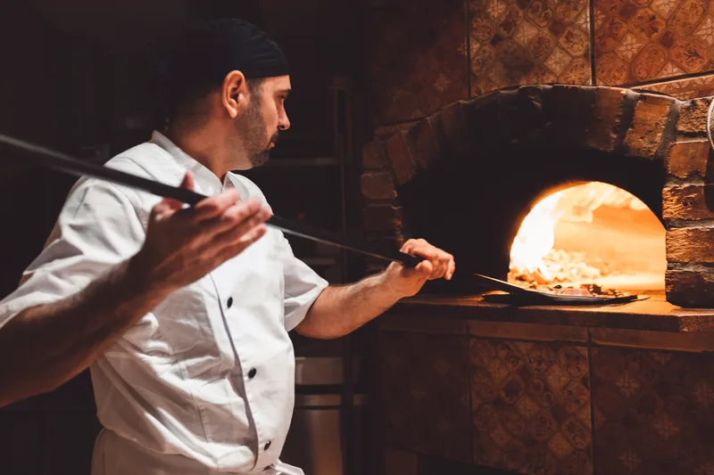Pizza maker sliding a pizza into a wood-fired oven