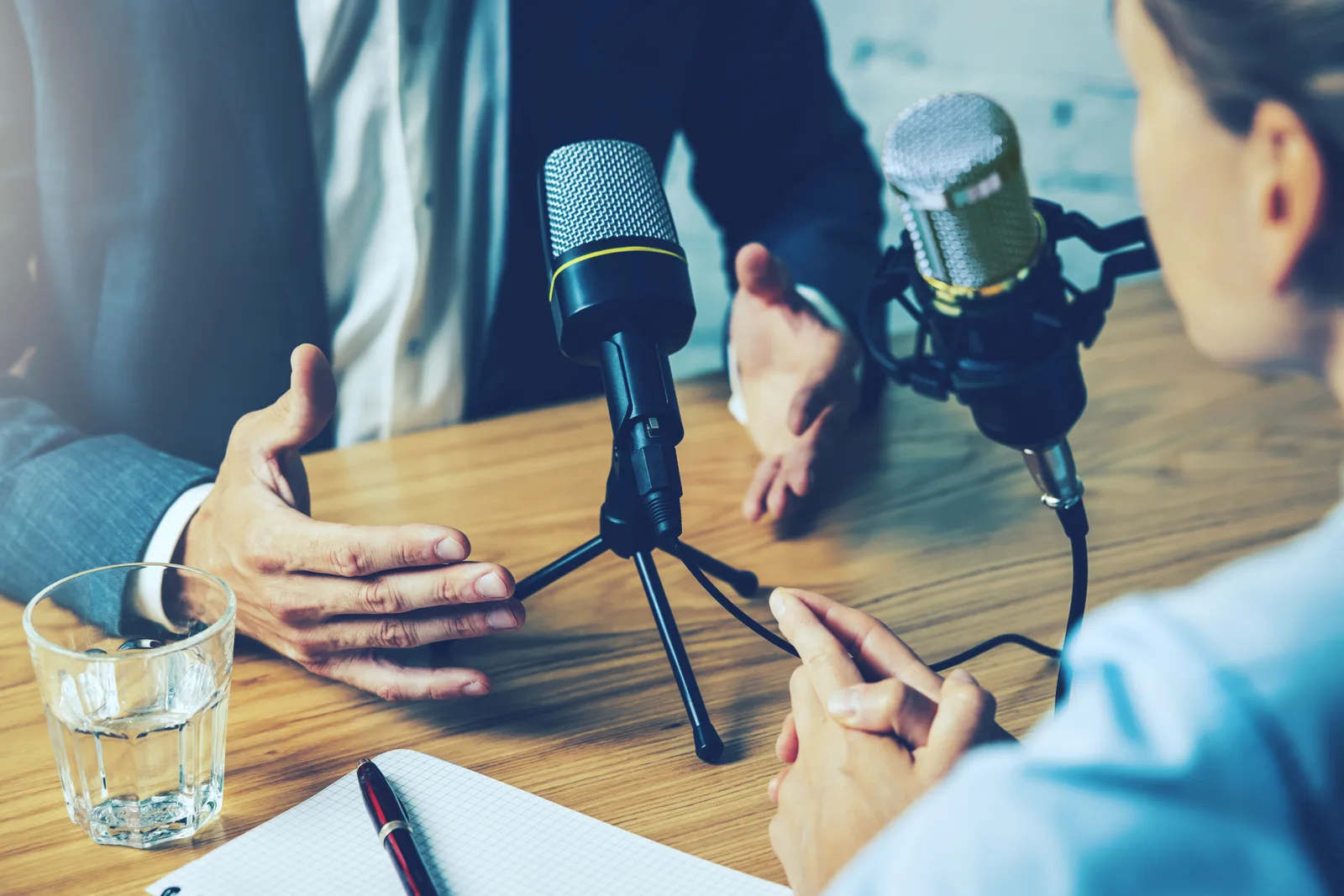 Two podcast hosts recording an episode together in a studio, each speaking into a microphone with headphones on