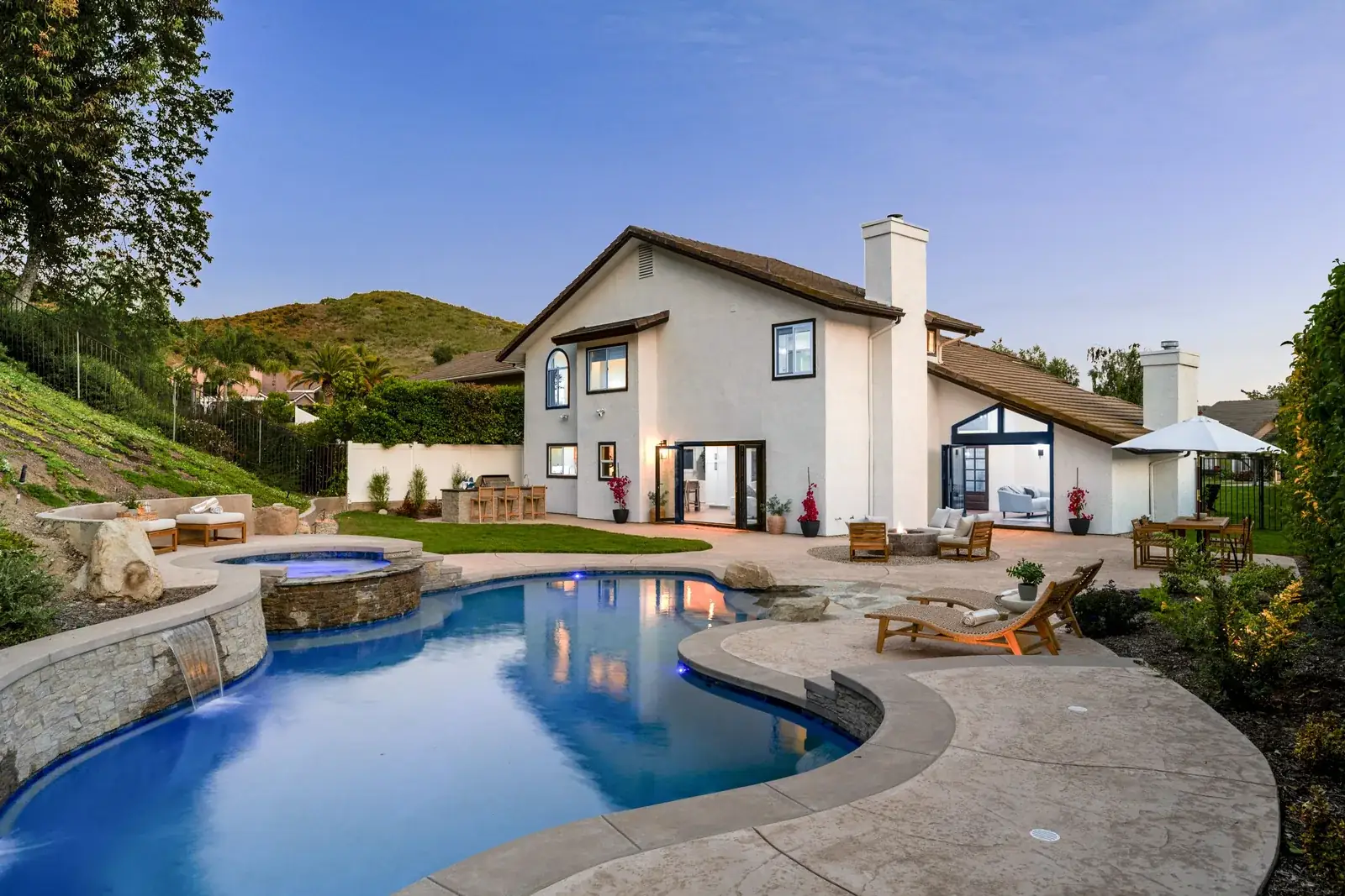 Newly finished inground pool and patio glowing at dusk in a fully landscaped backyard