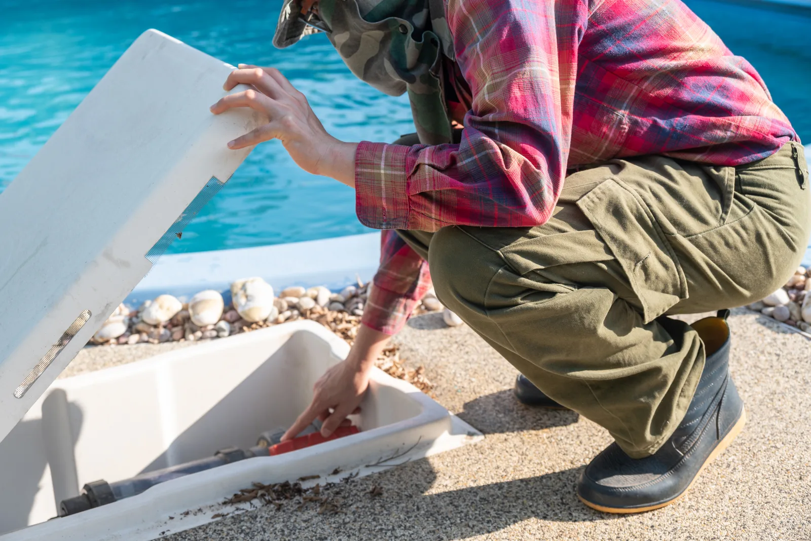 Pool service technician skimming debris from a backyard pool and checking water chemistry with a test kit