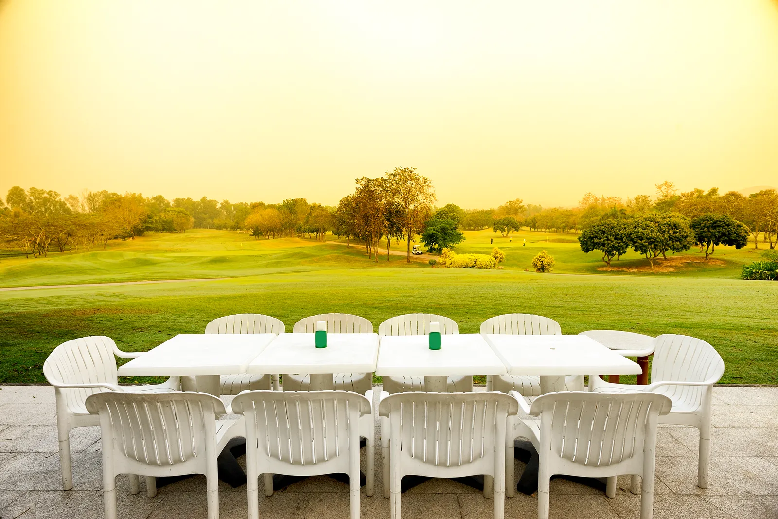 Elegant clubhouse terrace at a private country club overlooking manicured golf greens at golden hour