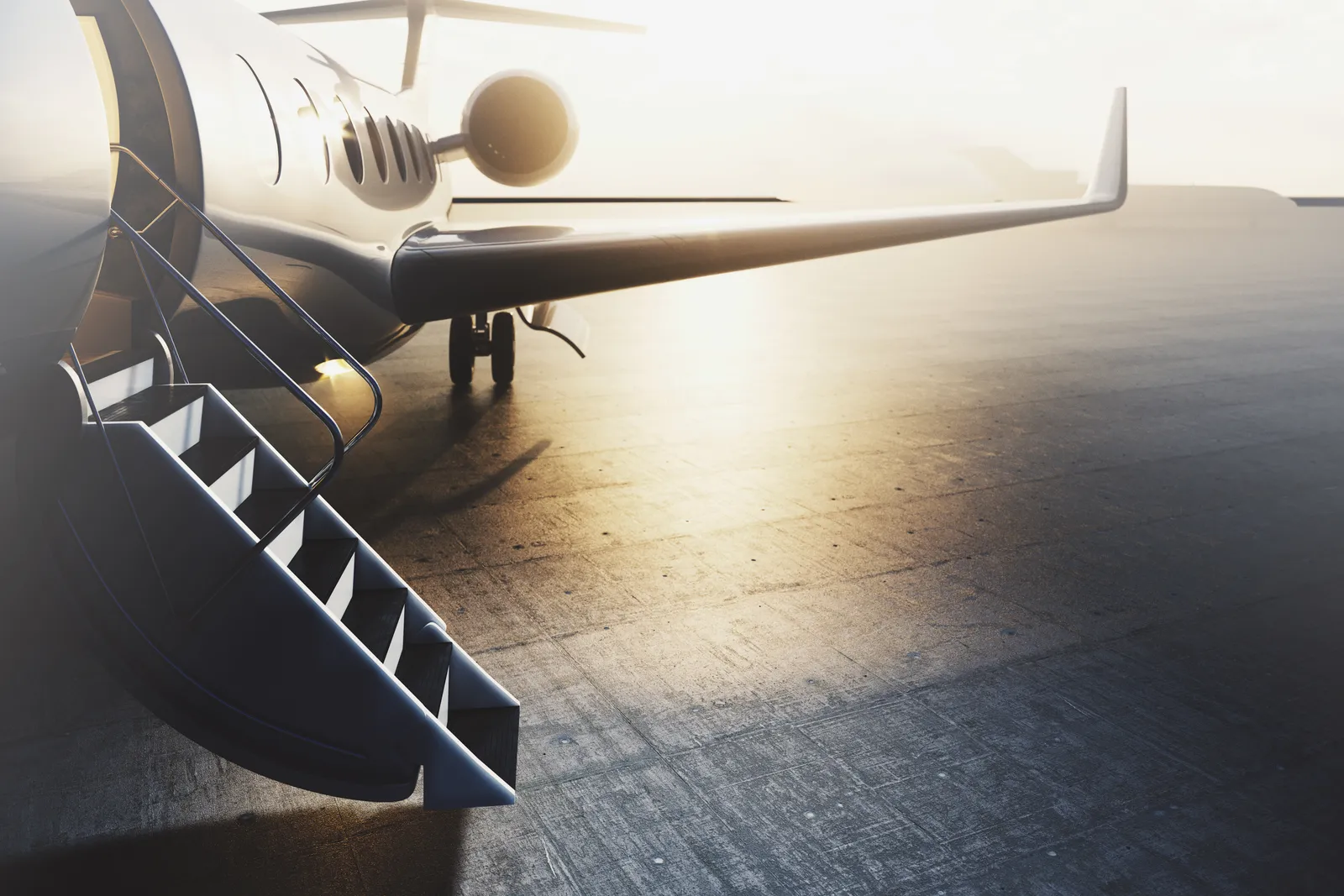 Private jet parked on the tarmac at dusk with airstairs down, ready for boarding