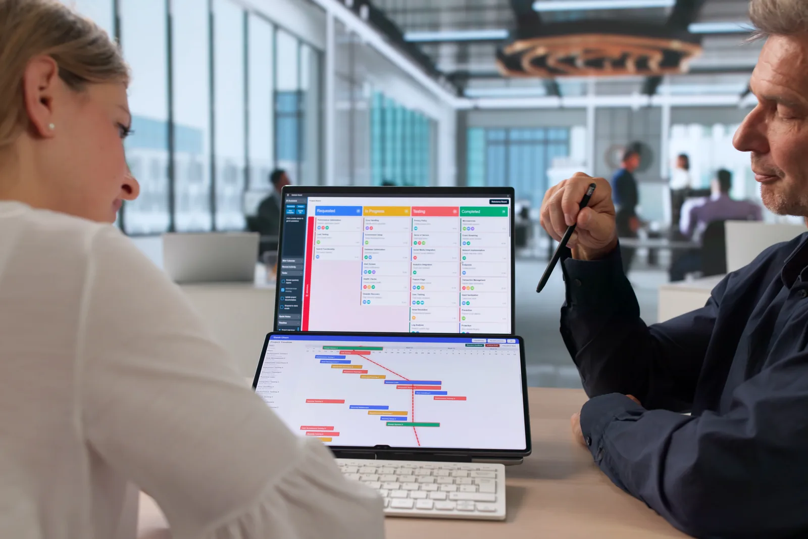 Project management software team reviewing a project board and trial-signup dashboard together at a laptop in their office