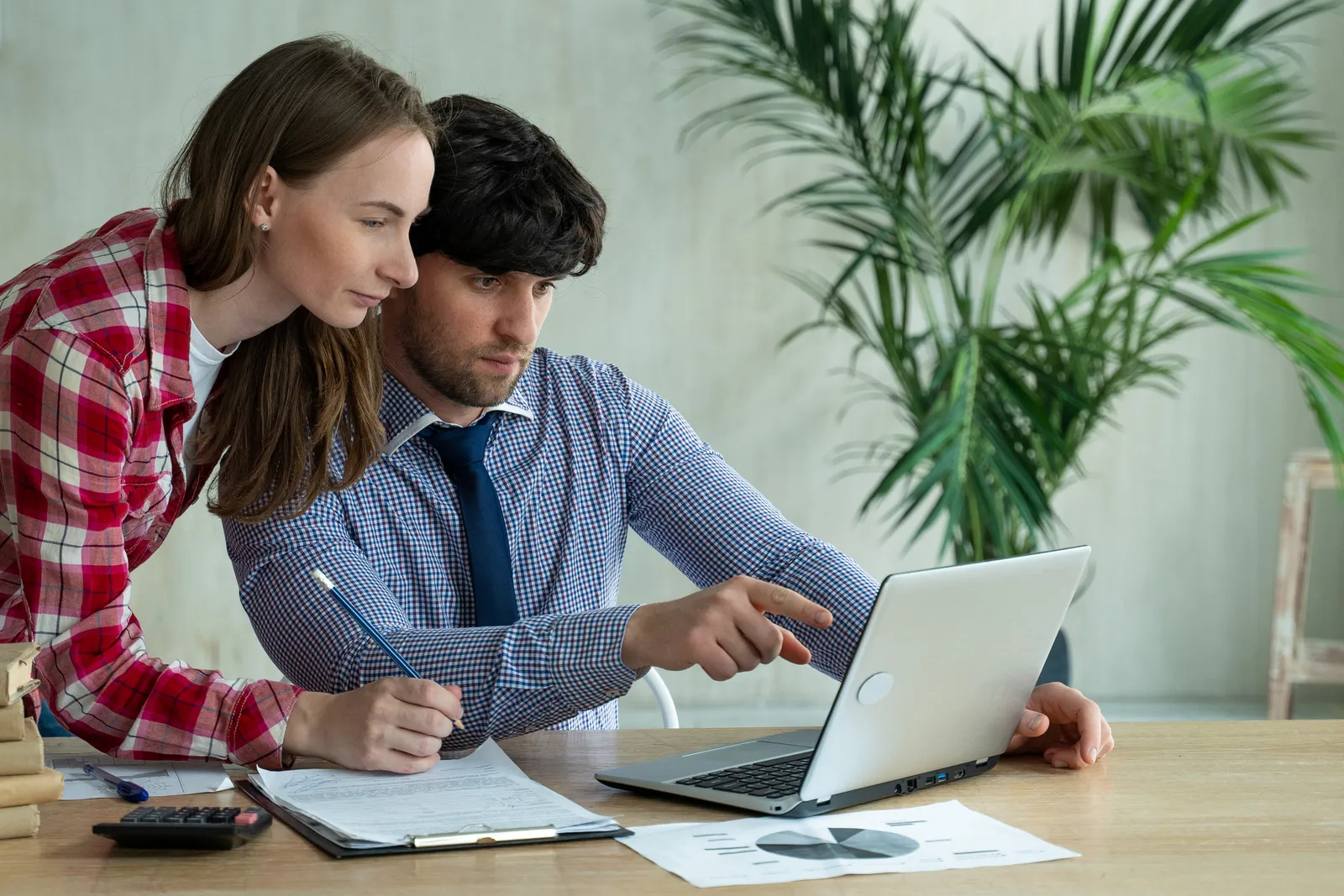 Two colleagues at a laptop reviewing a sales proposal with a pricing table and e-signature field on screen