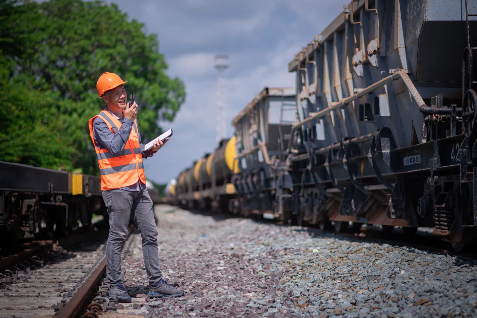 Railroad worker in a safety vest radioing beside freight cars in a rail yard