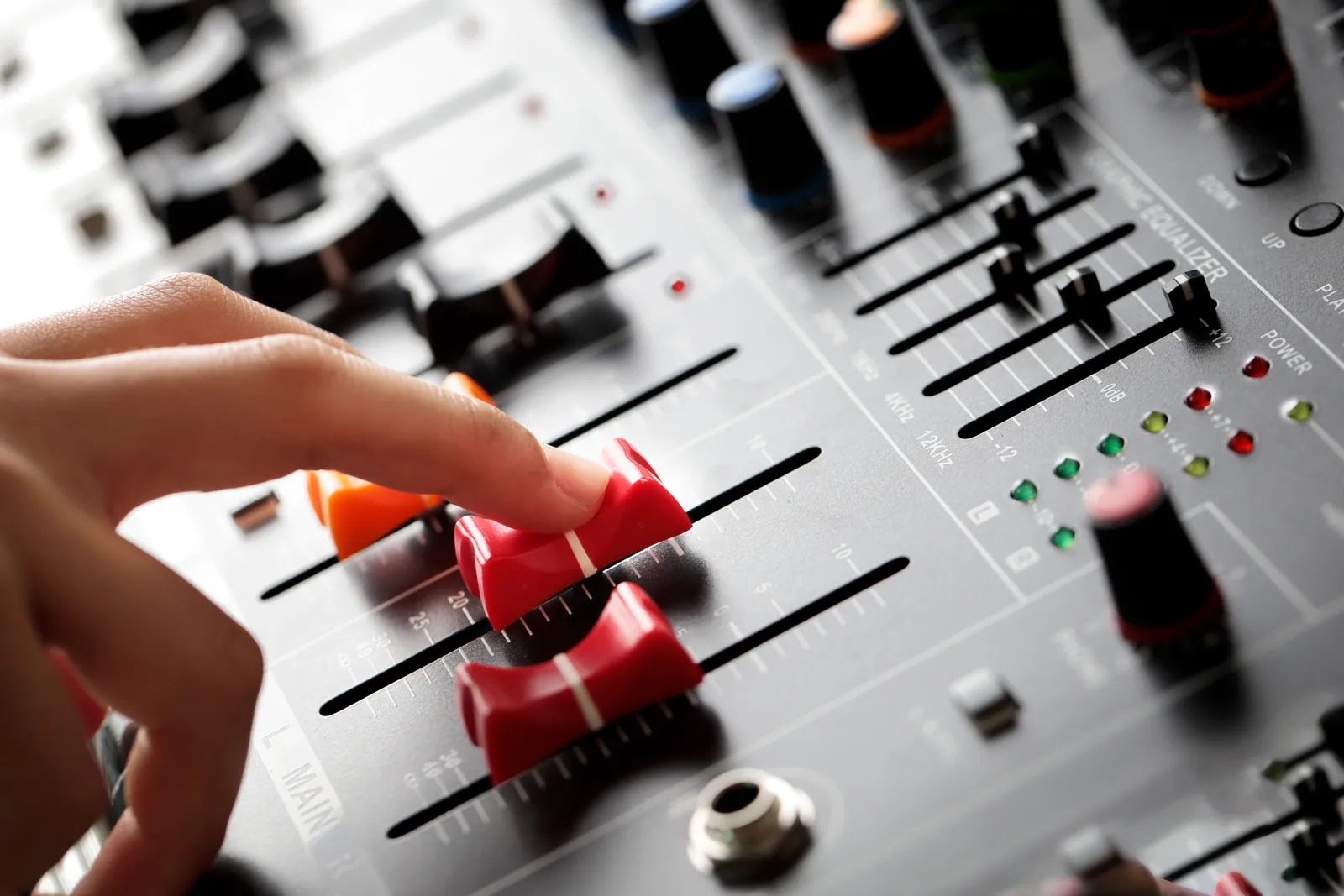 Hand adjusting faders on a studio mixing console