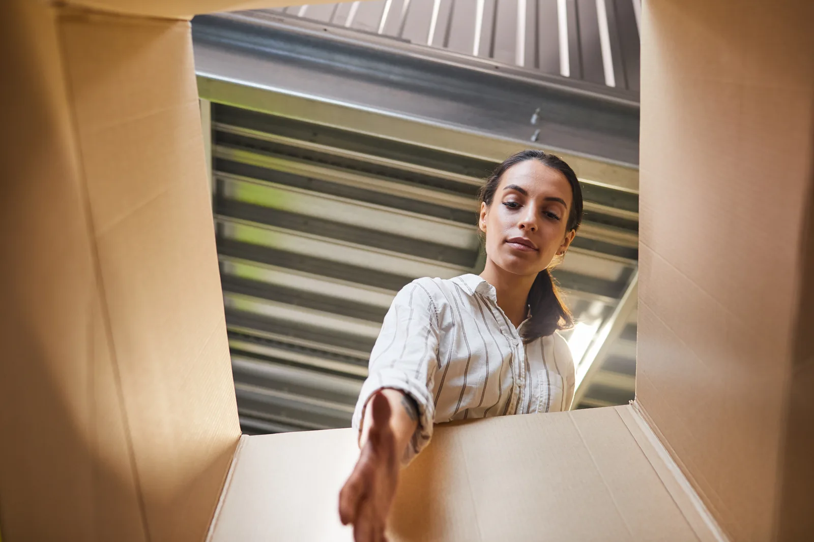 Renter wheeling a dolly of boxes past a row of bright orange roll-up doors at a self storage facility