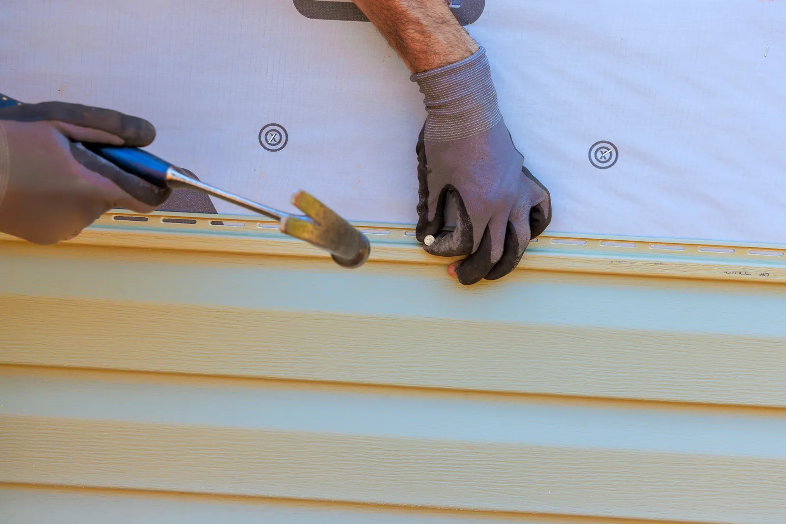 Contractor fastening new horizontal siding panels to the exterior wall of a suburban home
