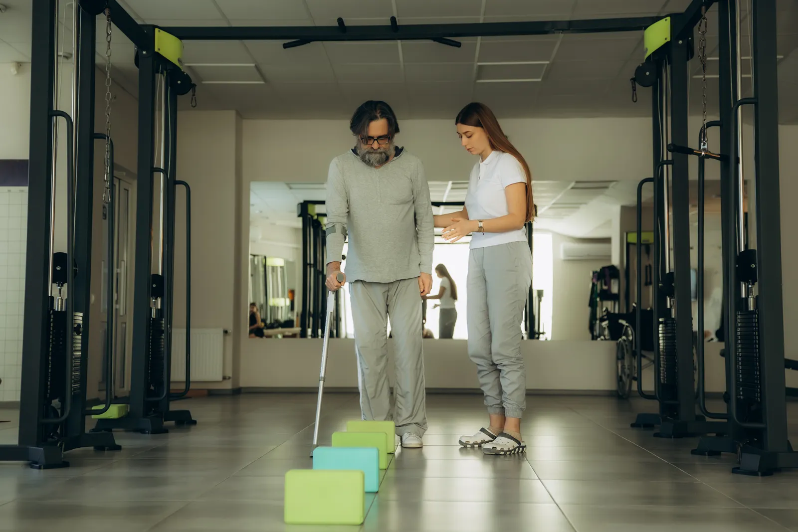 A physical therapist helps a skilled nursing facility resident practice walking with a walker in a rehab therapy gym