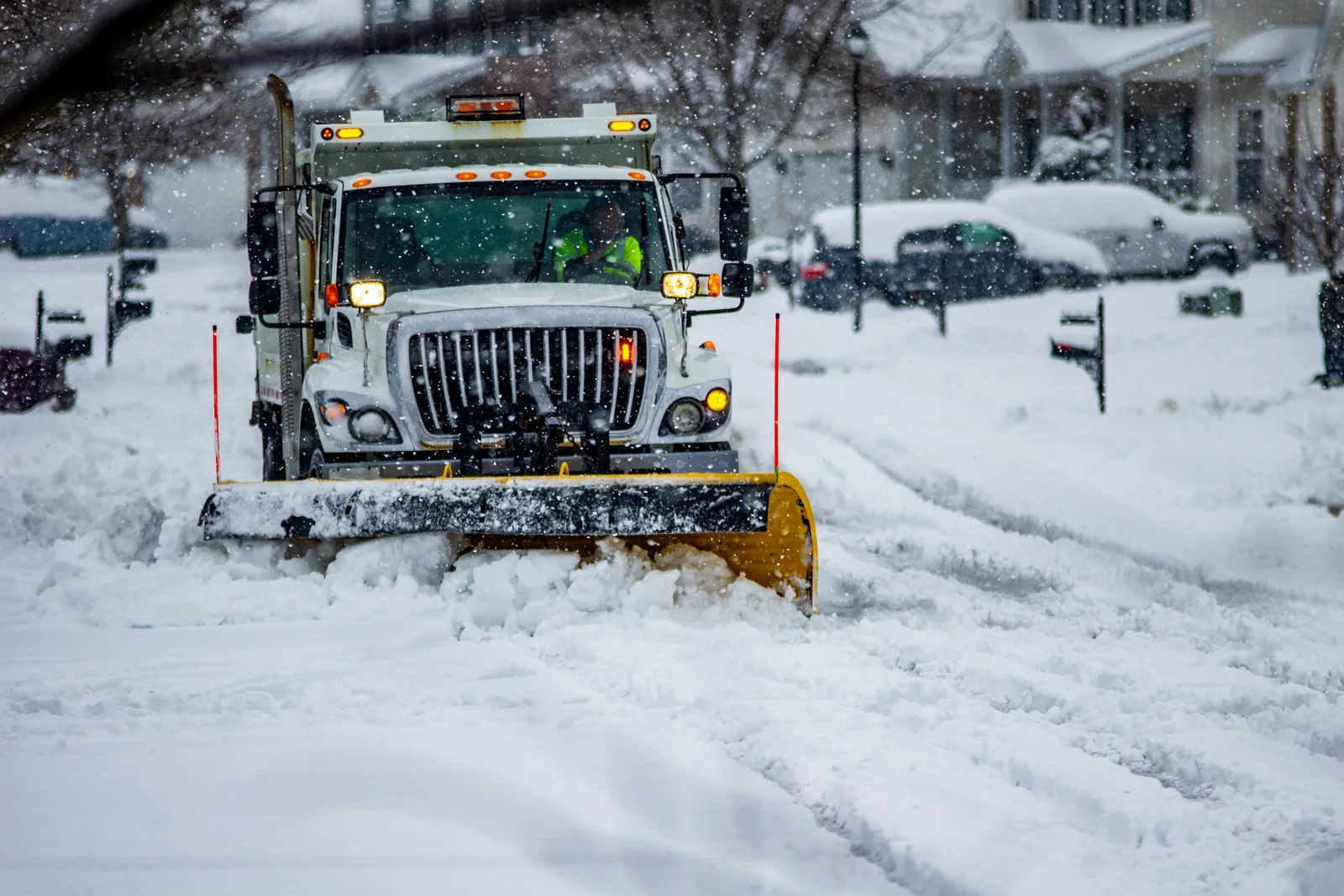 Snow plow truck clearing a snow-covered residential street during a winter storm