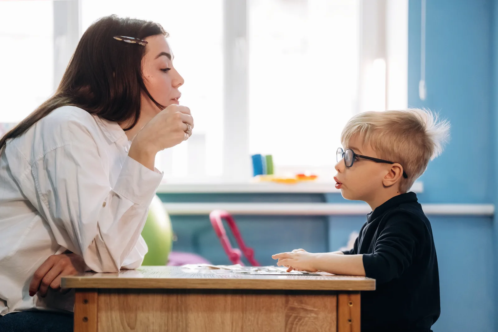 A speech-language pathologist working one-on-one with a young child at a table during a therapy session