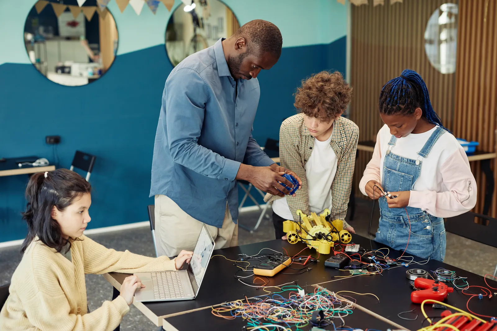 Instructor helping a small group of elementary-age students assemble and program a robotics kit at a STEM enrichment center worktable