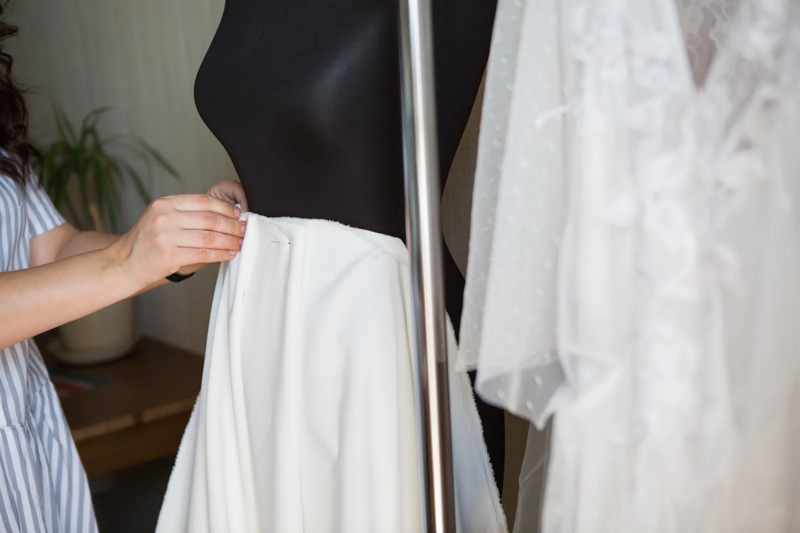 Tailor pinning the hem of a wedding dress on a mannequin while marking adjustments with tailor's chalk