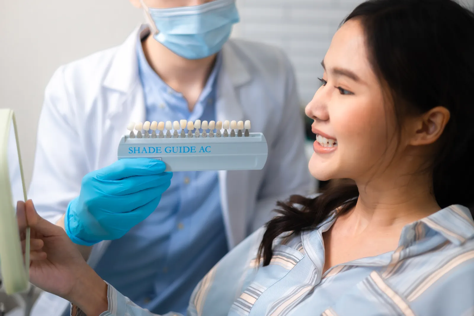 Clinician comparing a tooth shade guide with a patient's smile at a whitening studio