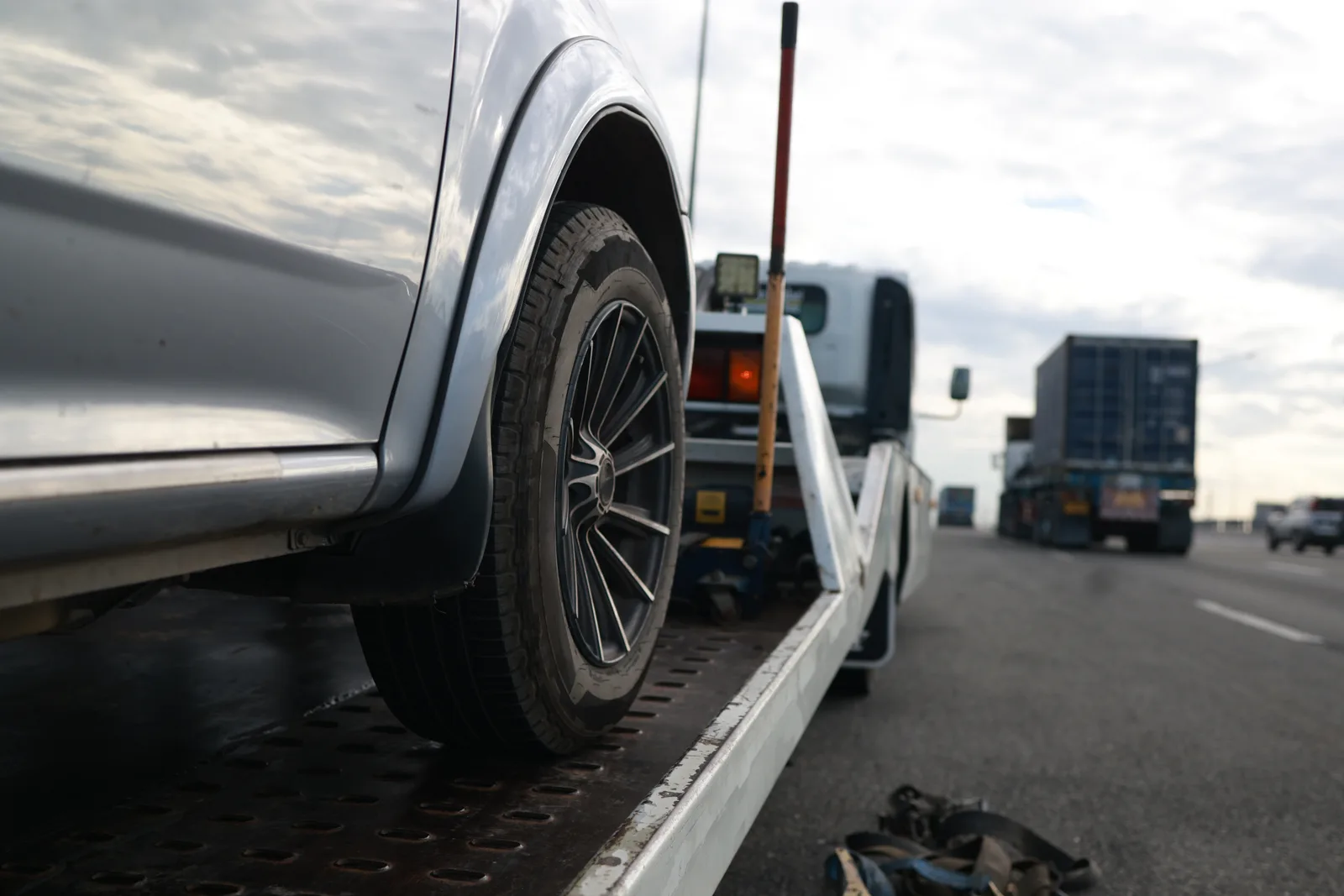 Tow truck operator winching a disabled sedan onto a flatbed at the roadside