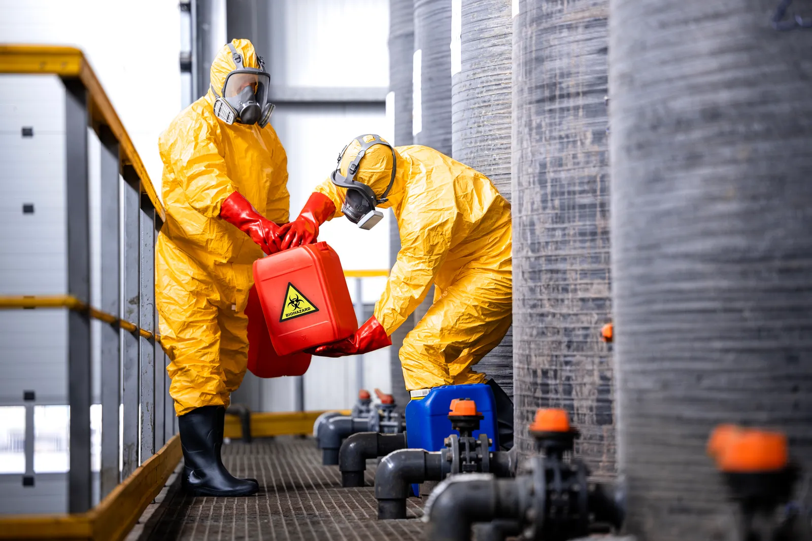 Workers in protective hazmat suits handling a chemical container at an industrial site