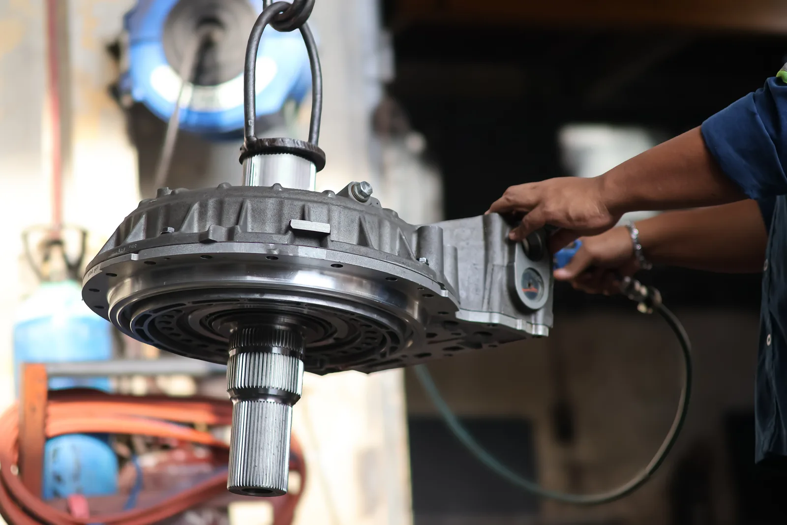 Technician's hands guiding a transmission into place on a hydraulic lift in a repair shop bay