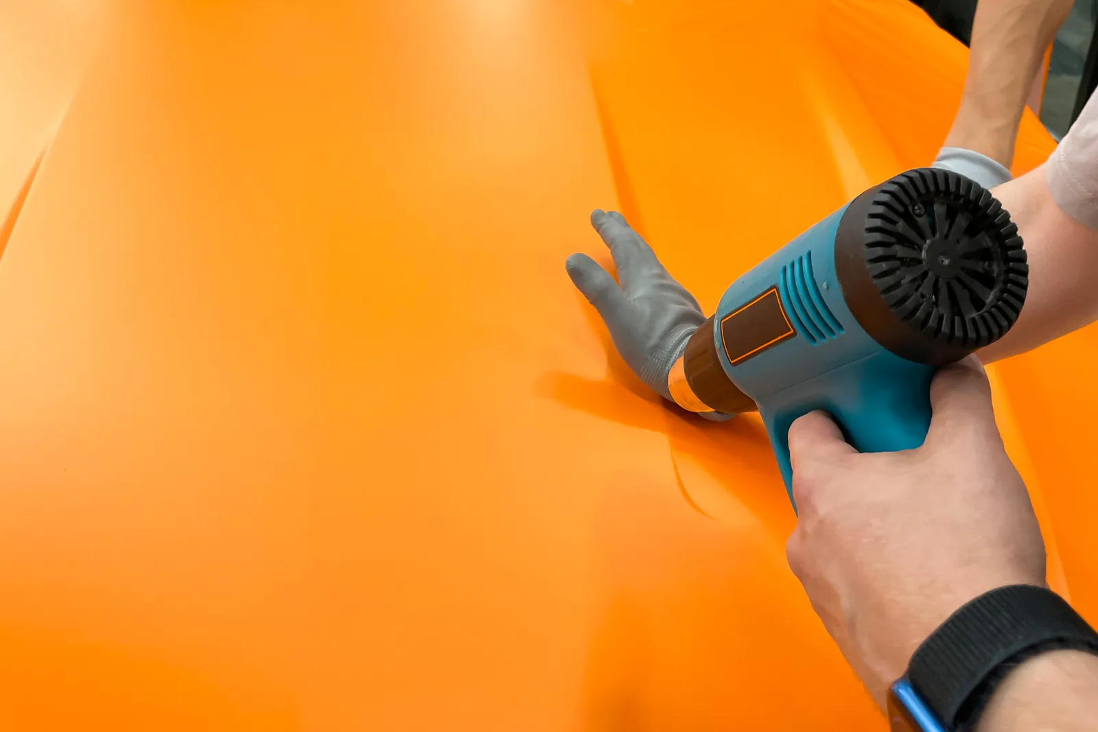 Installer using a heat gun and squeegee to apply a vinyl wrap film to a car's rear quarter panel