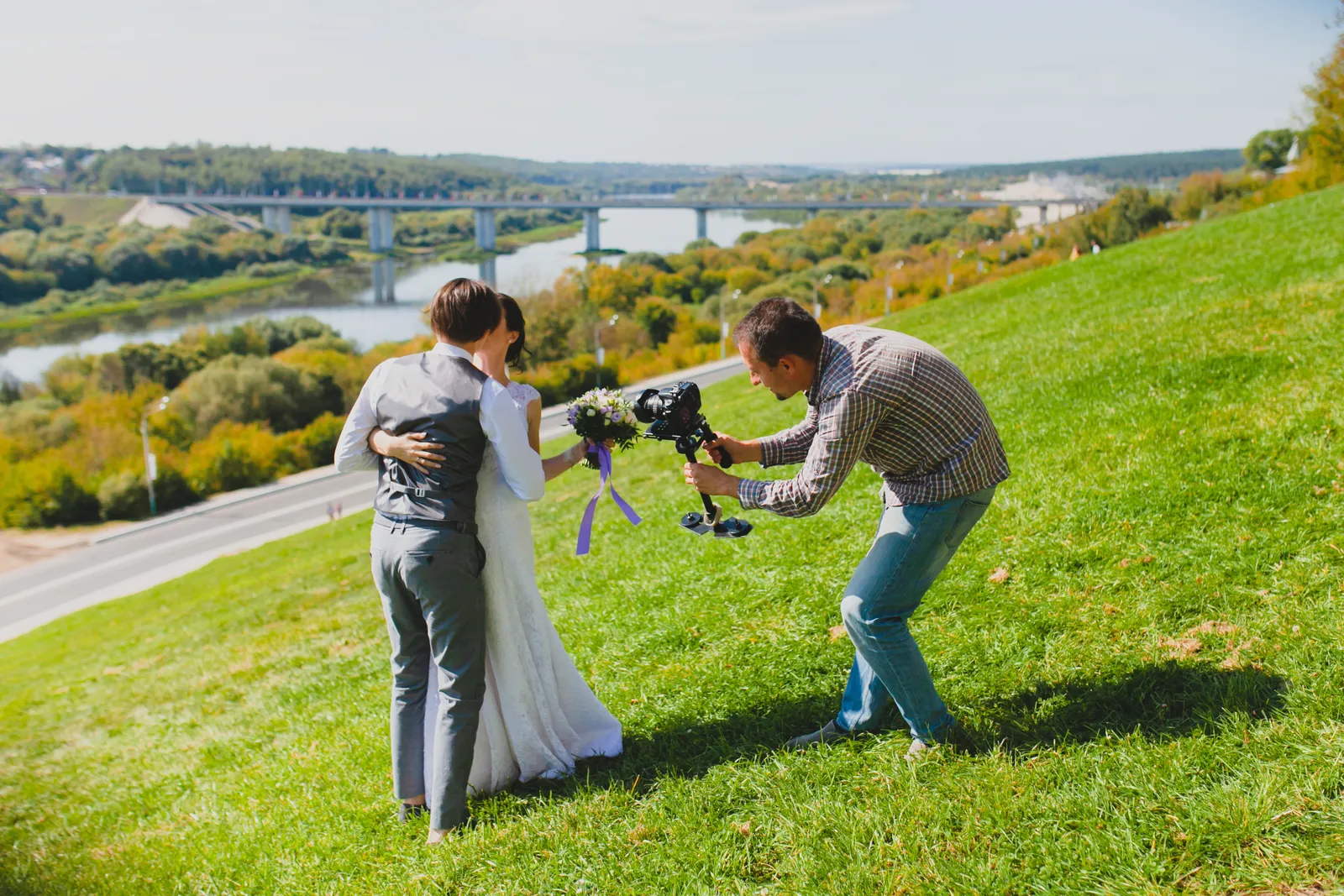 Videographer holding a cinema camera on a gimbal while filming a couple during an outdoor wedding ceremony