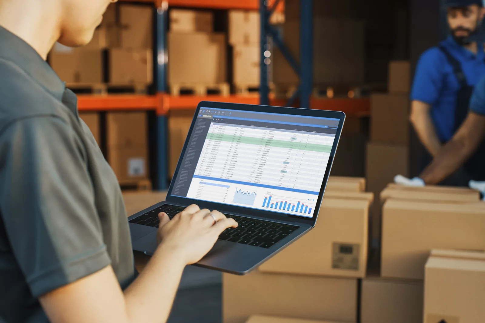 Warehouse operations manager reviewing inventory and order-fulfillment dashboards on a laptop on the warehouse floor