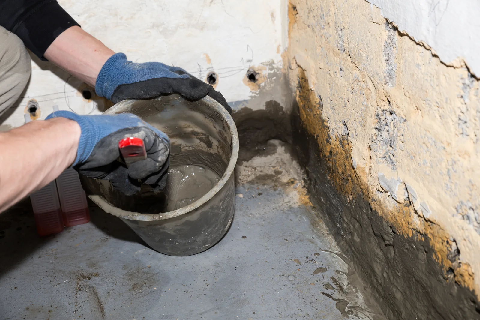 Waterproofing technician installing an interior French drain and sump pump basin along a basement wall