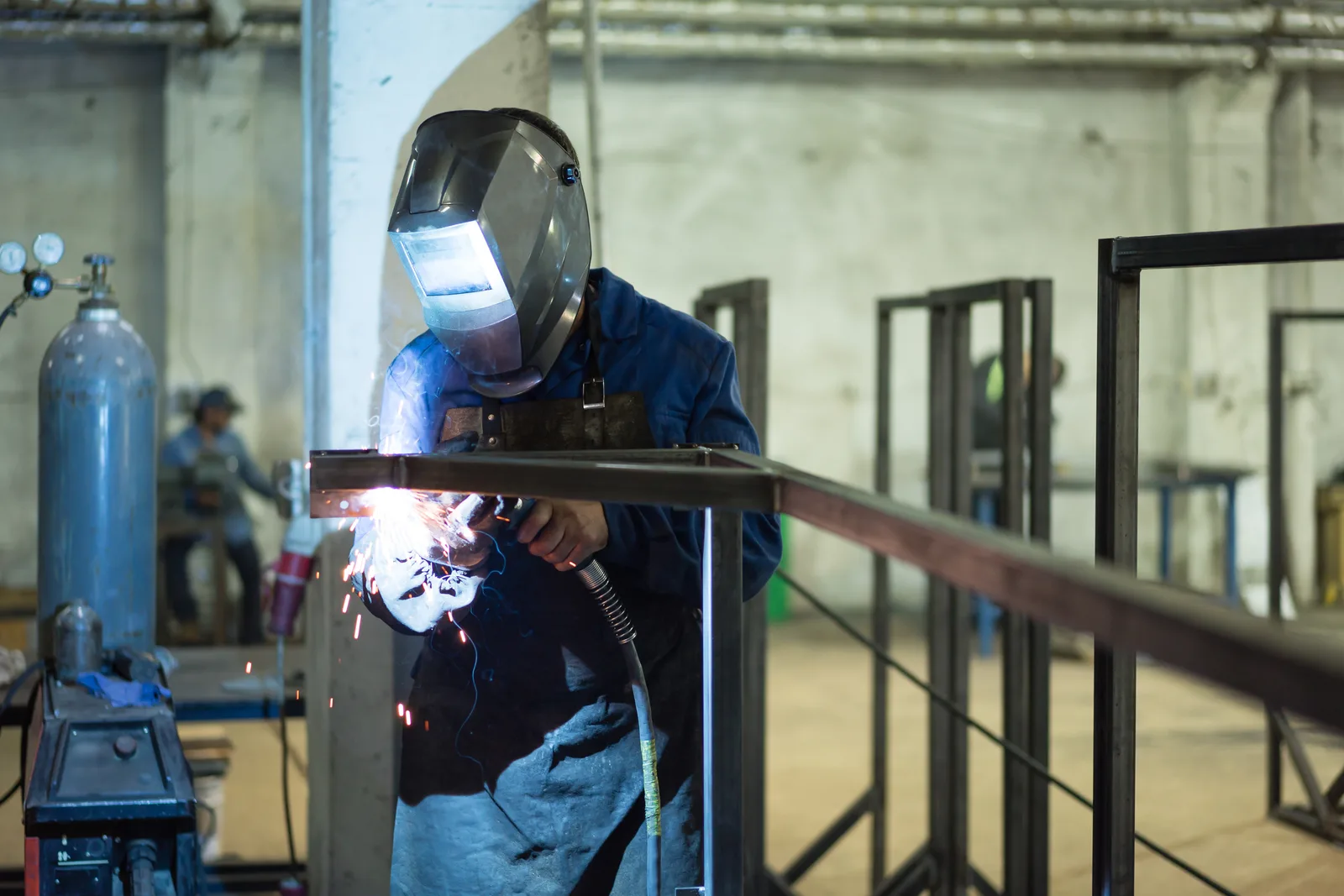 Welder in protective gear and helmet fabricating a custom metal railing in a fabrication shop