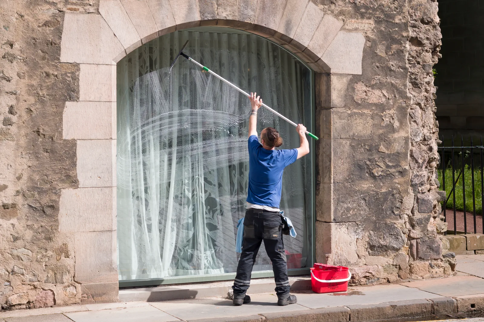 Window cleaner using a squeegee to clean a large exterior window on a two-story home