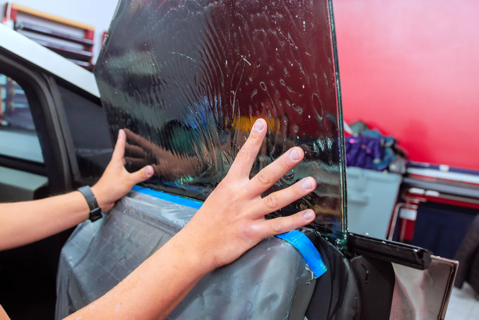 Tint installer smoothing dark film onto a sedan's rear window with a squeegee inside the shop bay