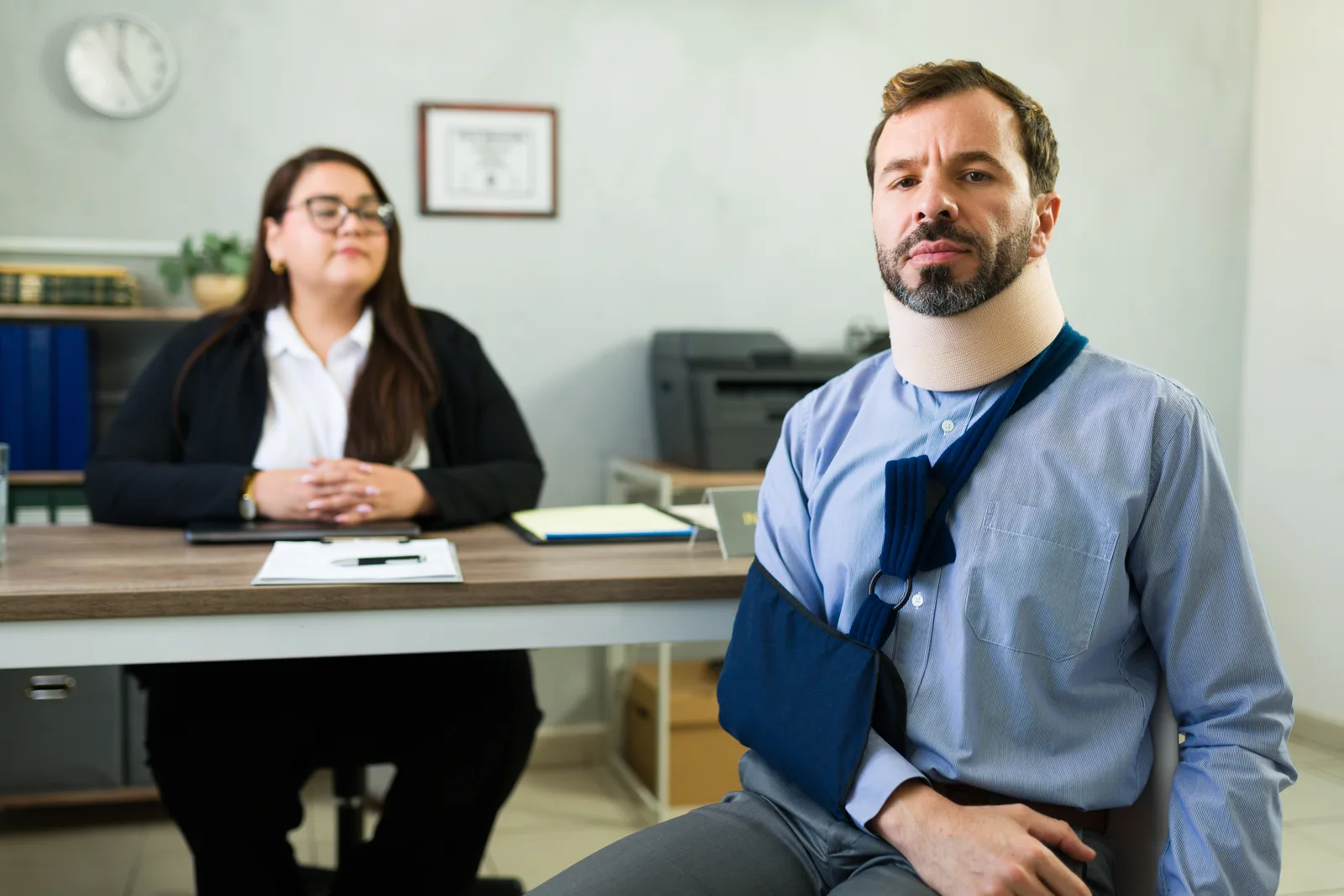 Workers' comp attorney reviewing a denied-claim file with an injured warehouse worker whose arm is in a sling