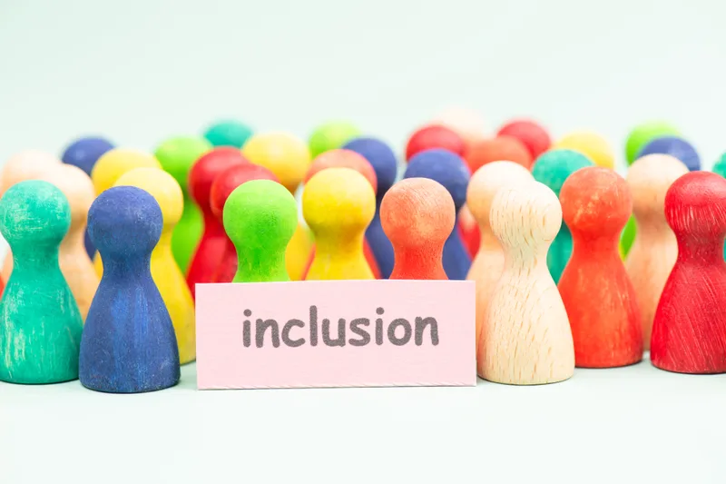 Dozens of colorful wooden figures gathered around a small card that reads 'inclusion'