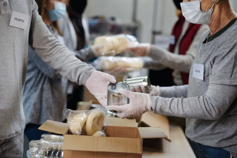 Gloved volunteers passing canned goods down a sorting line over open donation boxes of bread and produce