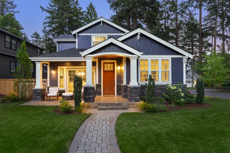 Craftsman-style two-storey home with stone pillars, a covered porch and a manicured lawn at dusk