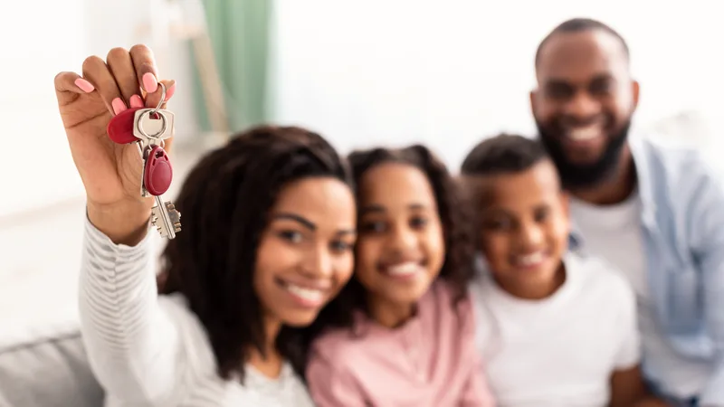 A smiling family of four holding up the keys to their newly purchased home
